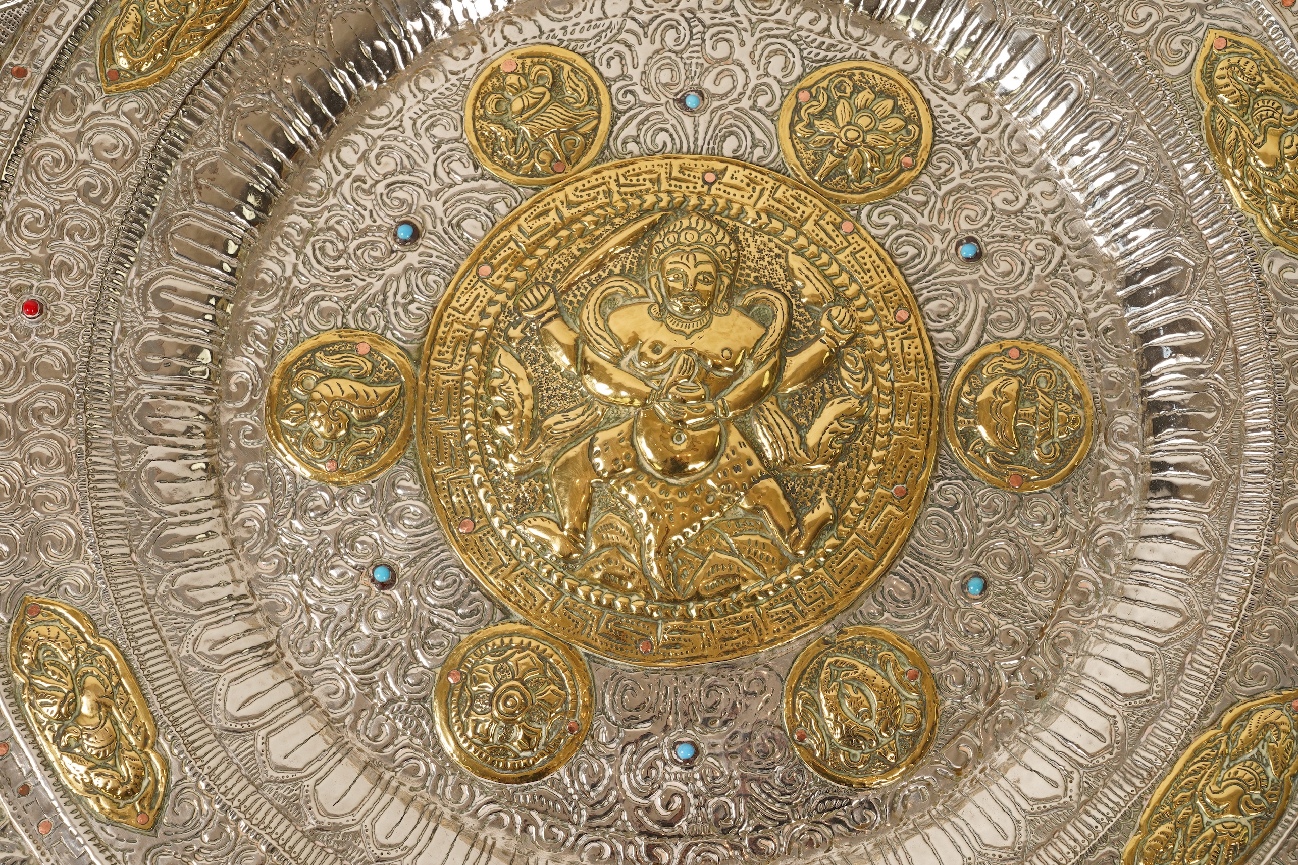 A graduated set of three Nepalese repoussé white metal and brass chargers, first half 20th century